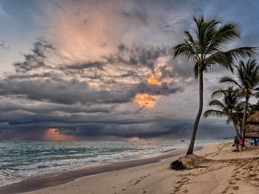 Dramatic storm clouds over the beach at Punta Cana with palm trees swaying in the wind.